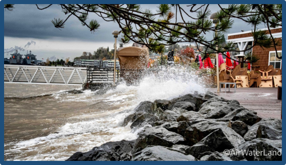 Wave crashing over beach barrier onto sidewalk during high tide. Wave crashing over beach barrier onto sidewalk during high tide.