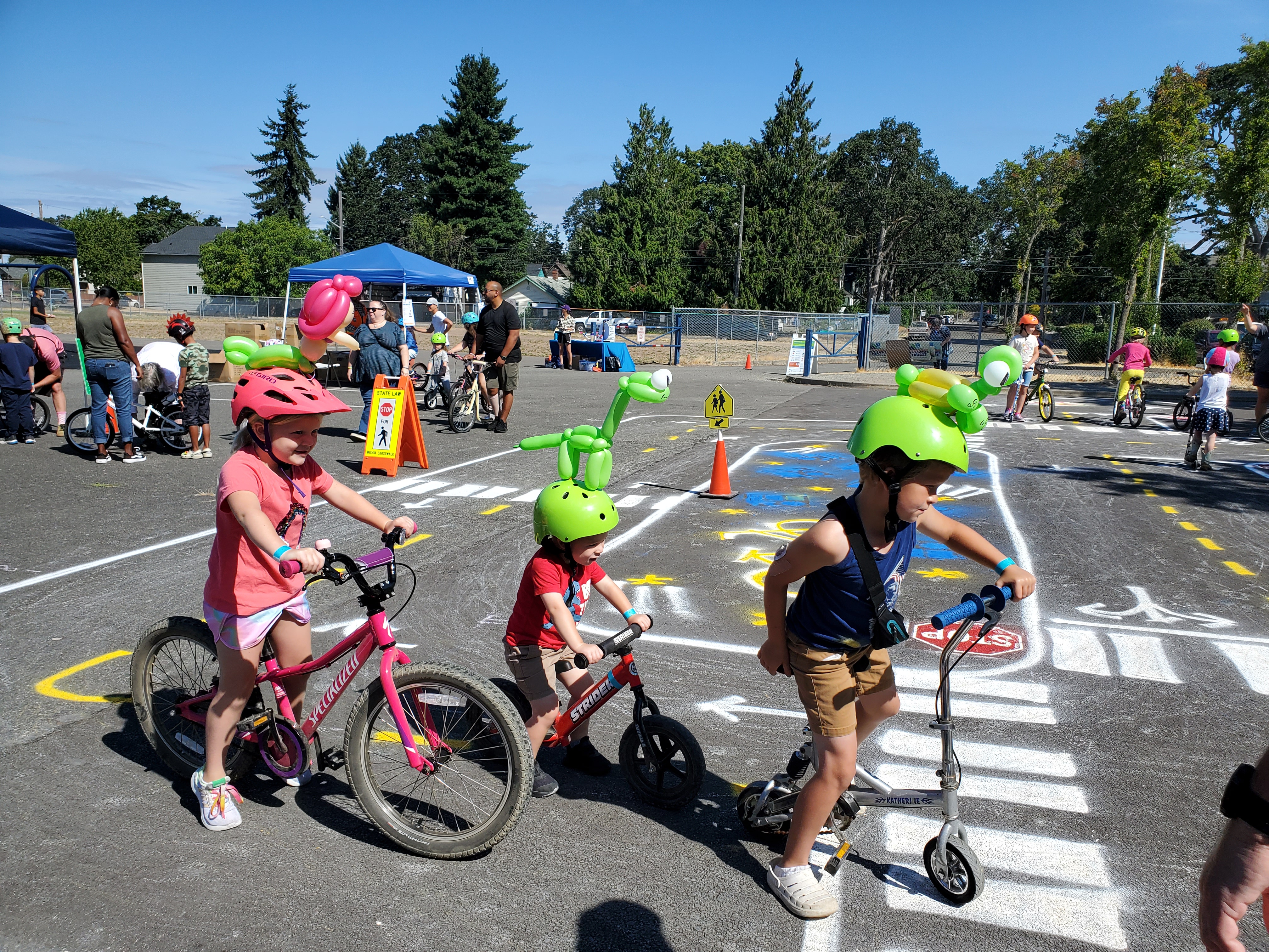 kids on bikes and scooters wearing bright colored helmets and practicing biking safety at a traffic garden. they are stopped at a 3-way stop intersection learning about stop signs and hand signals.
