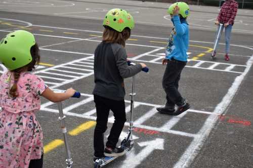 Youth practicing crossing the street as pedestrians and stopping and yeilding while on scooters at a traffic garden